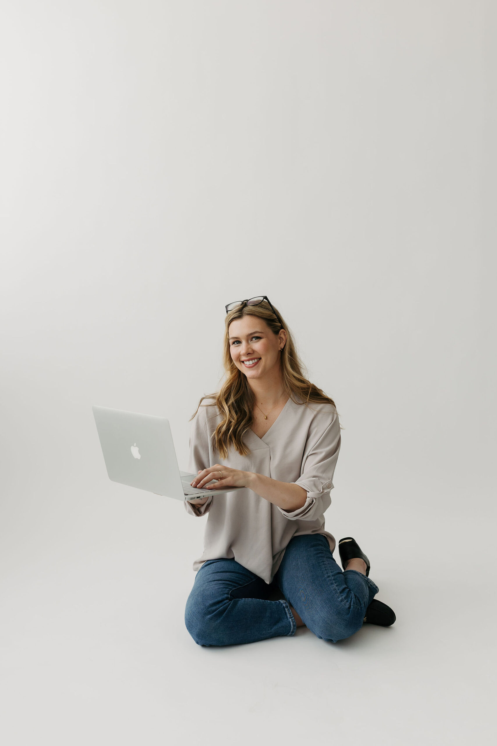 Woman kneeling on floor holding a laptop while smiling